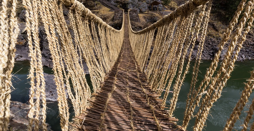 Visit the Q'eswachaka Bridge on your  Cusco tours! The Q'eswachaka Bridge is a hand-made suspension bridge, with four thick ropes serving as the main supports. You can  These ropes are woven from grass fibers and are anchored to stone abutments on either side of the river. Smaller ropes are then woven horizontally to create a walkway, and handrails are added for safety.